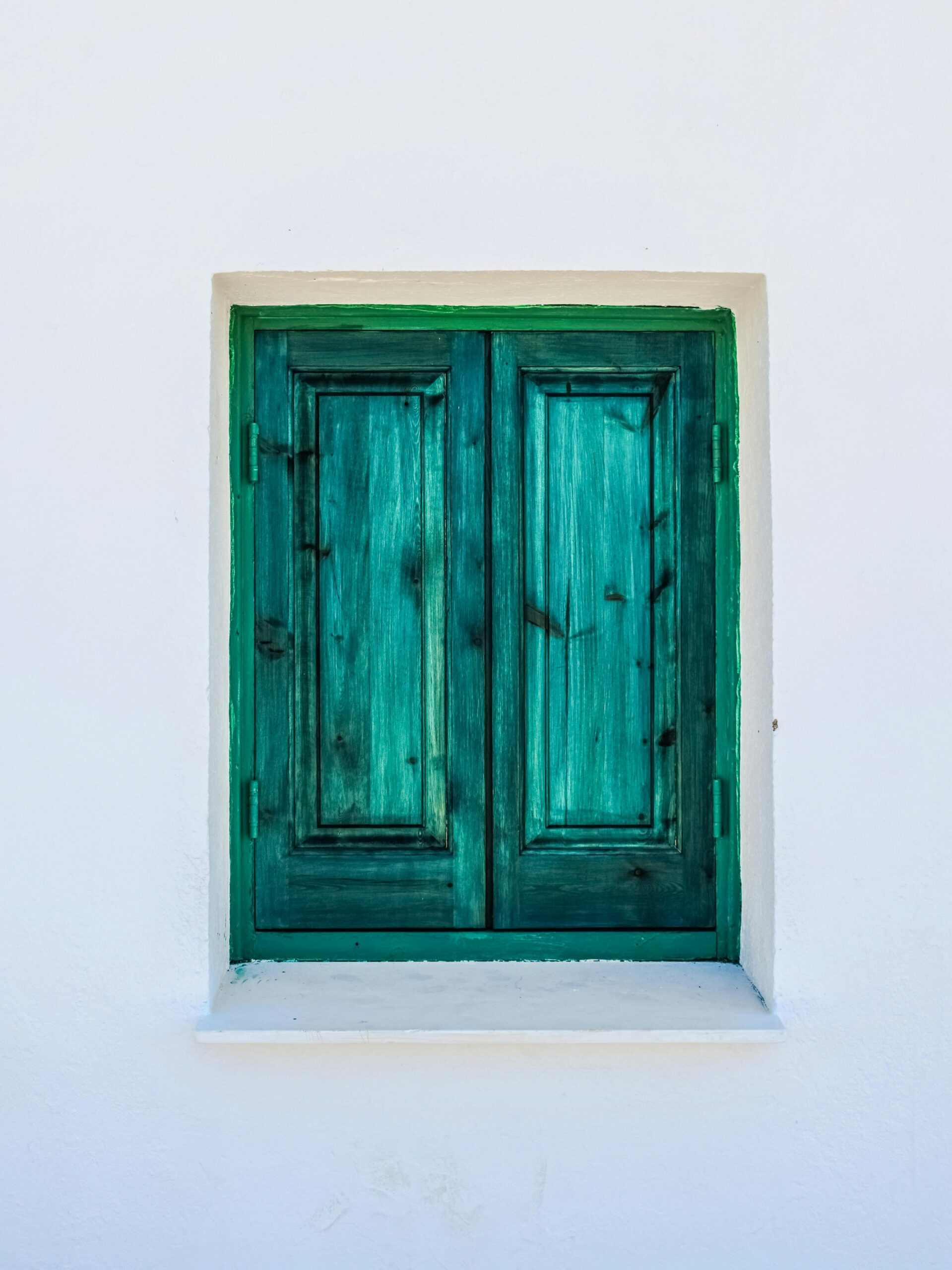 Retro green wooden shuttered window on a white exterior wall. Simple and classic.
